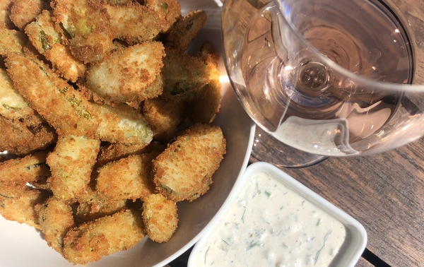 fried pickles in a white bowl beside a bowl of ranch sauce and a glass of rosé